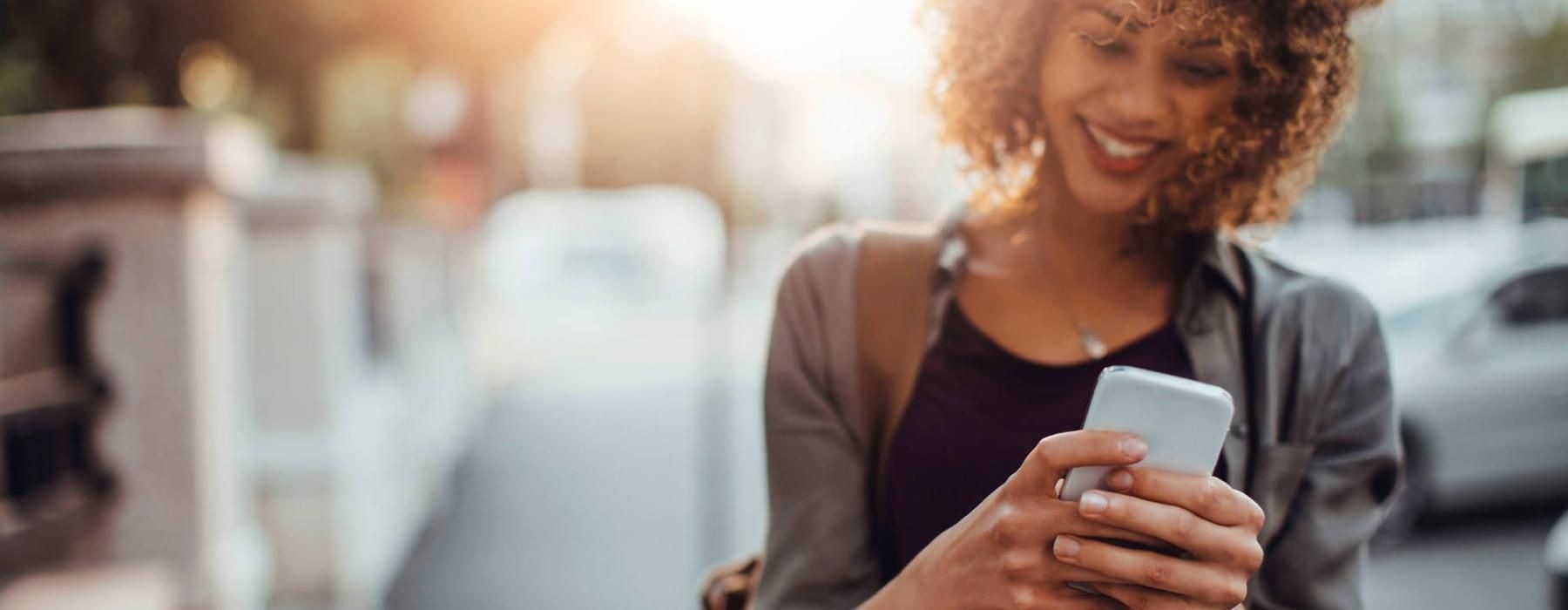 woman texts on her phone as she walks through the city