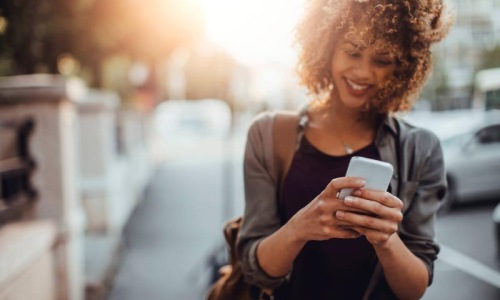 woman texts on her phone as she walks through the city